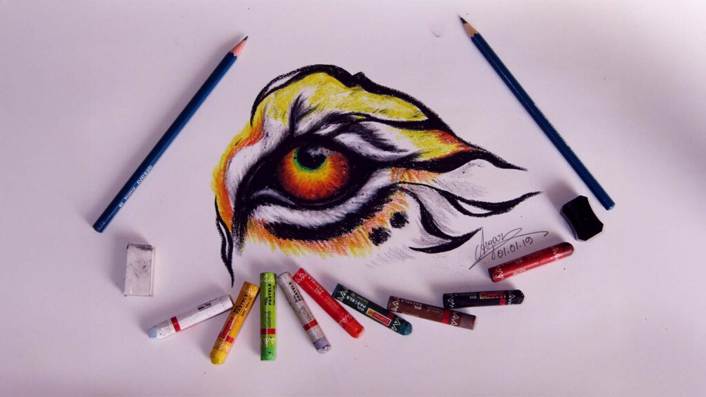 A vivid oil pastel drawing of the eye of a Royal Bengal tiger, surrounded by drawing tools on white paper.