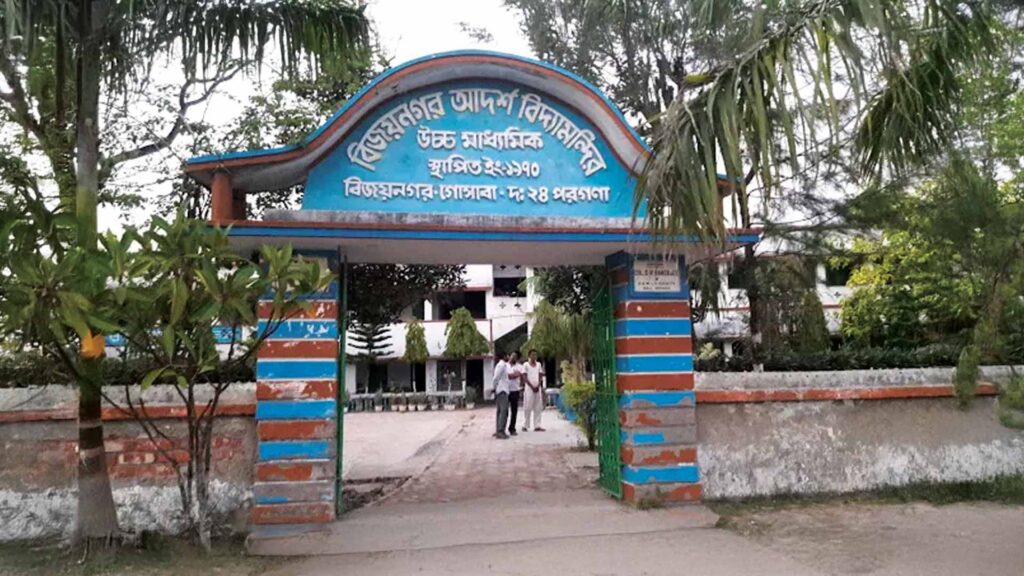 Front entrance of Bijoynagar Adarsha Vidyamandir (H.S) with a blue and orange striped gate and a visible school building in the background.
