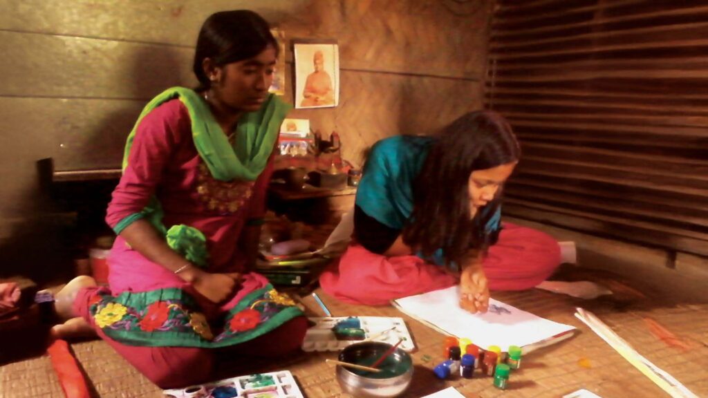 Bhaswati Patra and Moumita Mandal painting together inside a traditional village home.