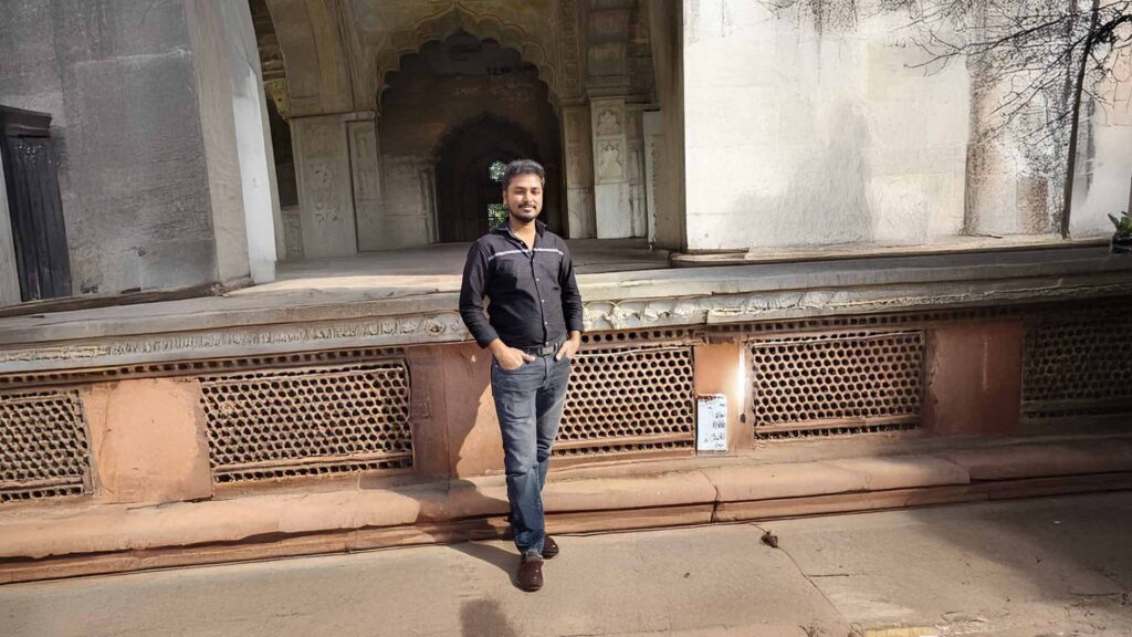 A man stands in front of an intricately carved Mughal-era structure inside the Red Fort complex.