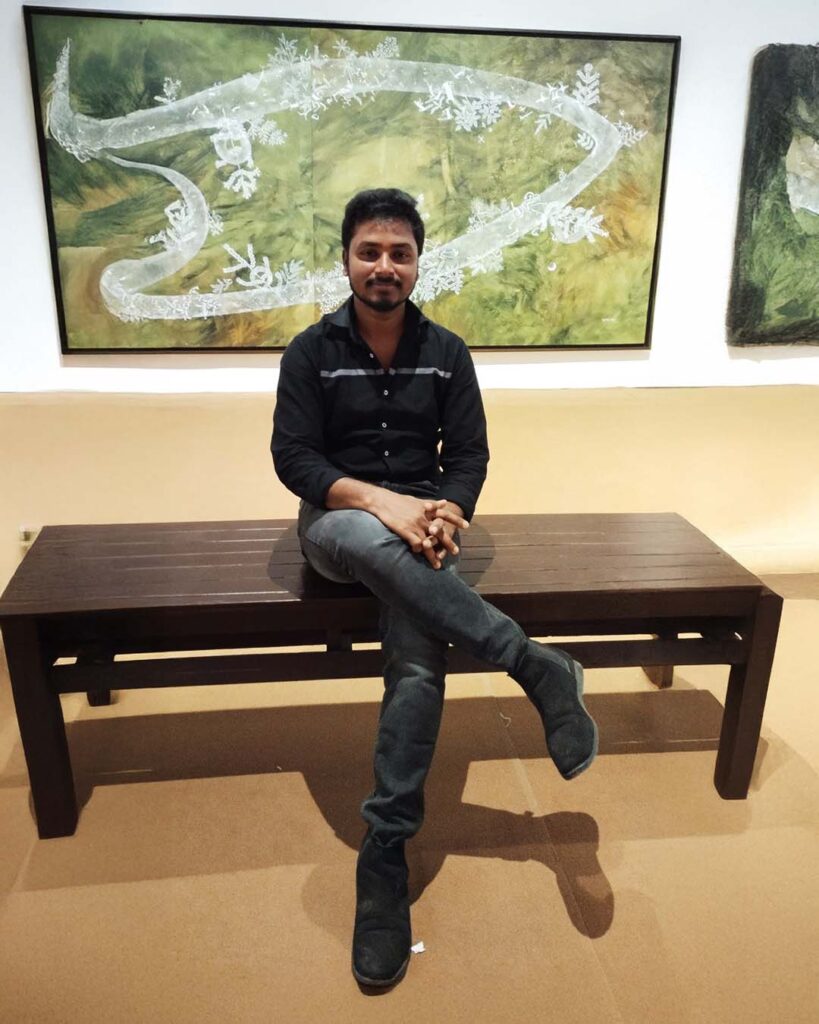A young man sits cross-legged on a wooden bench in front of a contemporary painting displayed in an art gallery.