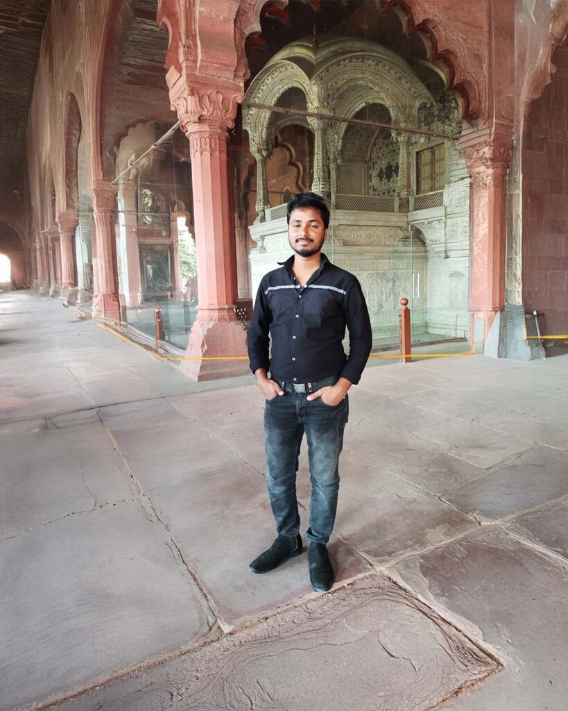 A young man stands inside the Diwan-i-Khas at Red Fort, with the ornate marble throne structure behind him.