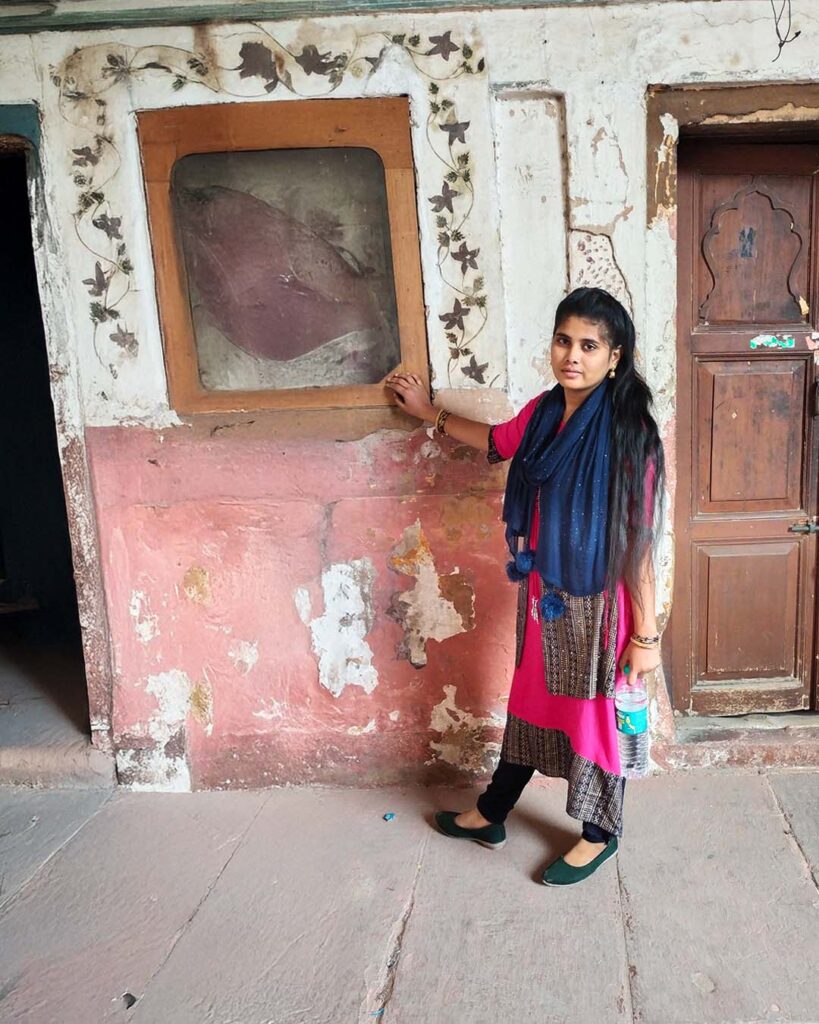 A young woman stands beside a framed historic artifact embedded in a wall at the Red Fort, Delhi.