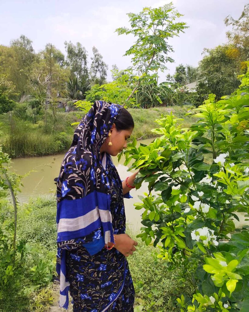 Tahamina Molla picking fresh leaves near a pond in her rural Sundarban garden.