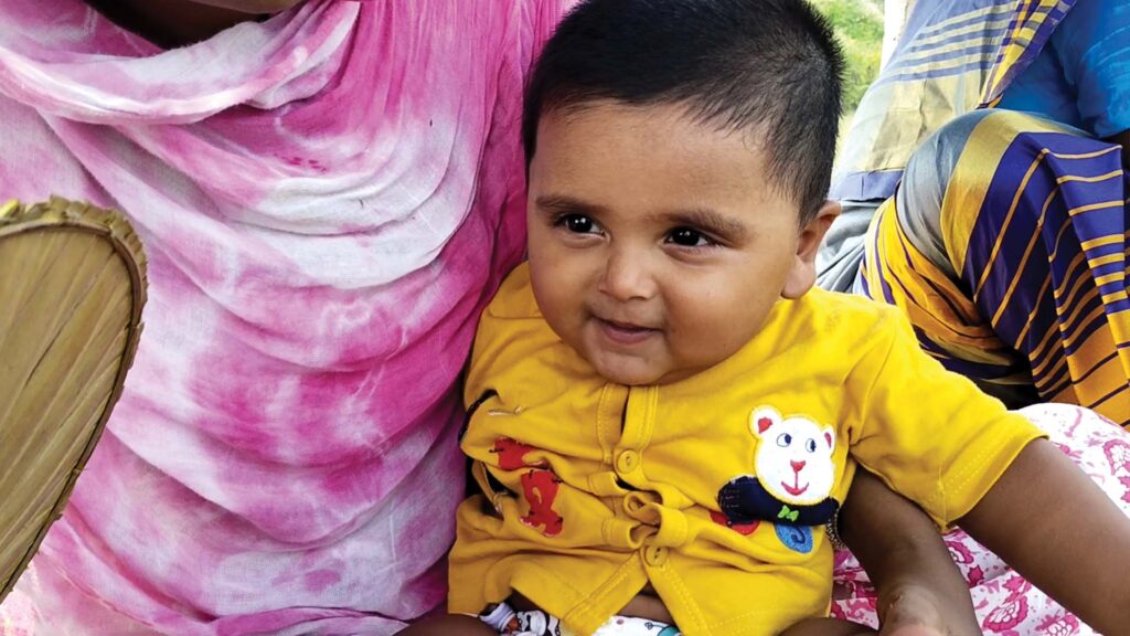 Smiling baby Arif Molla sitting on a family member’s lap during a Sundarban outdoor cooking vlog.