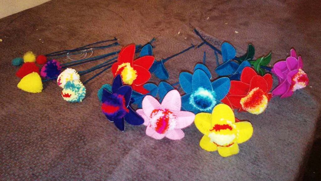 Handmade woolen flowers with colorful petals and stems laid out on a brown surface.
