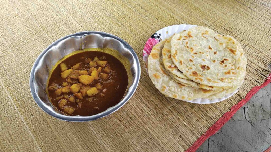 Traditional Bengali breakfast of golden parathas with spicy aloor dum served on a mat in Sundarban.
