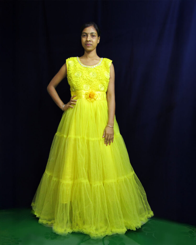 Amina Molla wearing a bright yellow gown, standing confidently against a dark background.