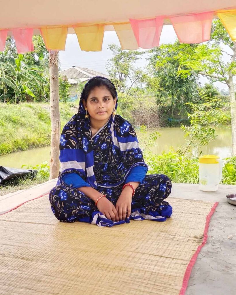 A Bengali woman sitting peacefully on a mat near a pond in rural Sundarban.