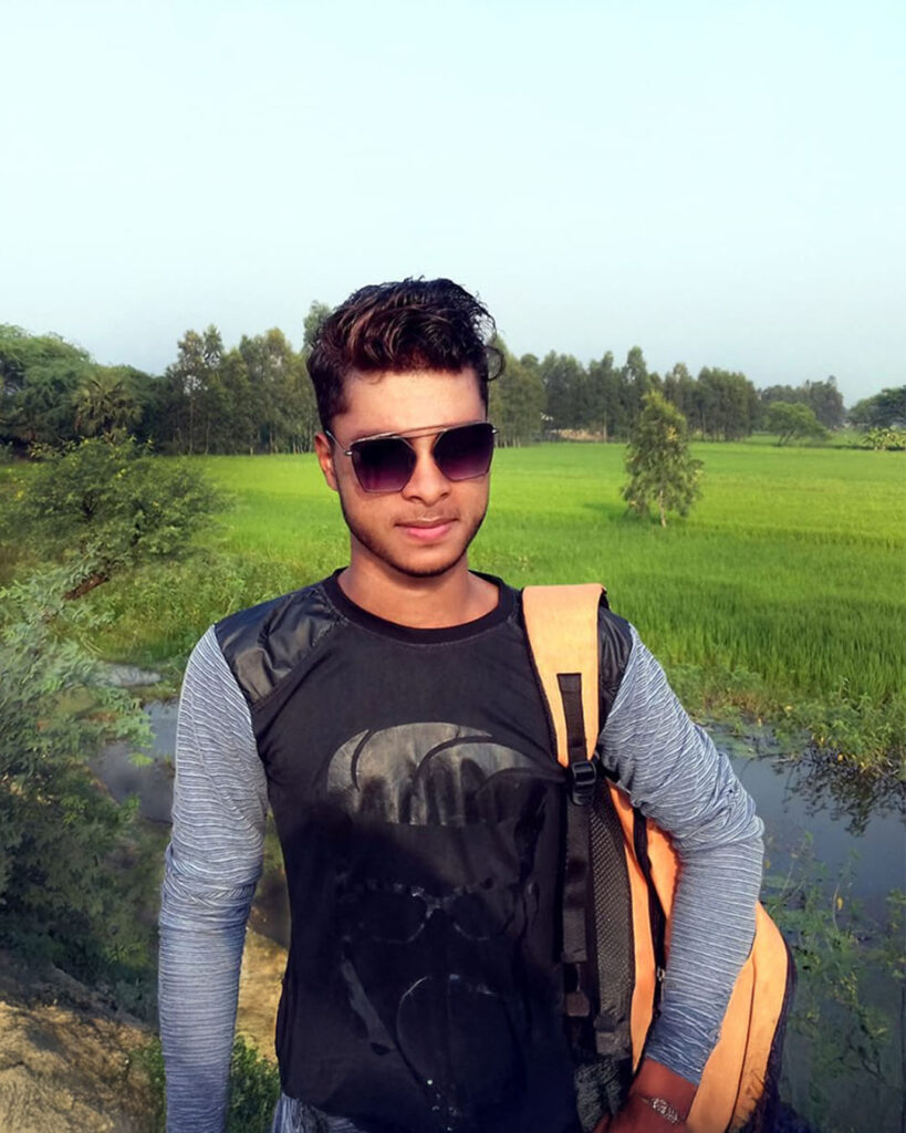 Ajahar Molla standing in front of a lush green field wearing sunglasses and a backpack.
