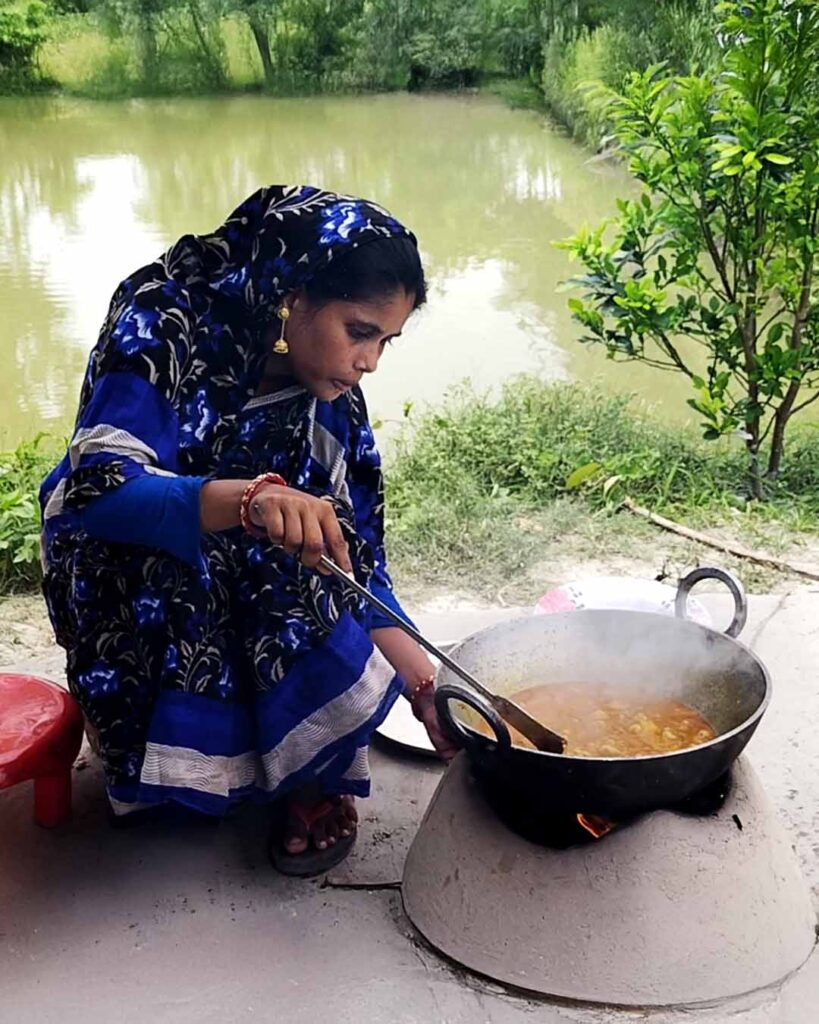 A Bengali woman cooking traditional Aloor Dum on a clay stove beside a pond in Sundarban.