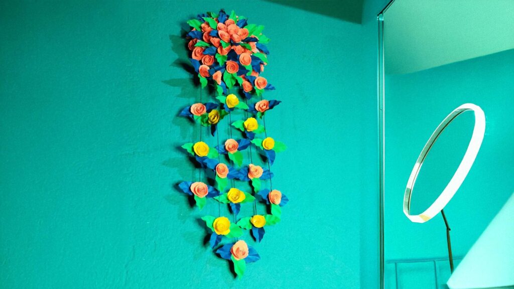Handmade paper flower wall art with orange and yellow roses on a turquoise wall