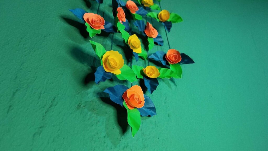 Close-up of handcrafted orange and yellow paper roses with green and blue leaves