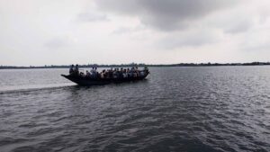 Crowded wooden boat ferrying passengers across a wide river in Gosaba, Sundarbans under a cloudy sky.