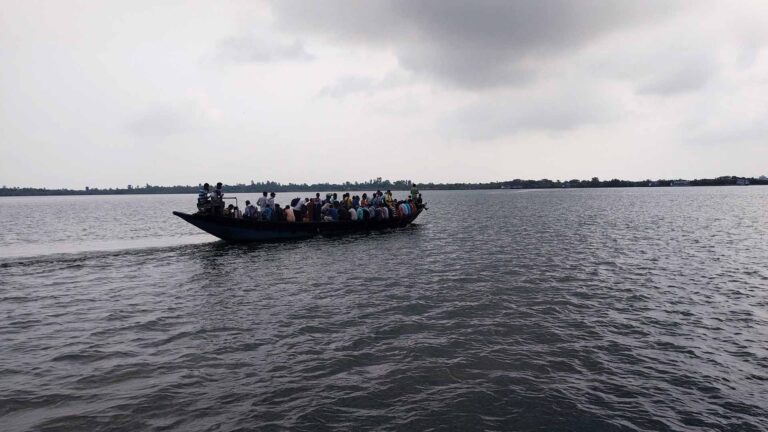 Crowded wooden boat ferrying passengers across a wide river in Gosaba, Sundarbans under a cloudy sky.